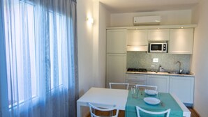 A compact kitchen with white cabinets, a microwave, and a dining area with a table and chairs. - Elbamar Lacona 2 - Elbamar Lacona 2 - Mono Classic (Capoliveri)