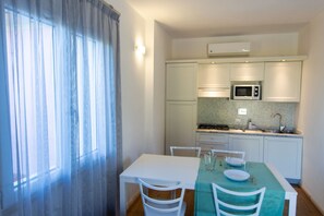 A compact kitchen with white cabinets, a microwave, and a dining area with a table and chairs. - Elbamar Lacona 2 - Elbamar Lacona 2 - Mono Classic (Capoliveri)