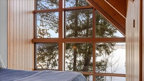 Una habitación con un ventanal grande que da a un bosque y una masa de agua.