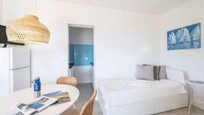 Ett modernt hotellrum med en säng, en matplats med bord och stolar, ett litet kök och en tavla på väggen.