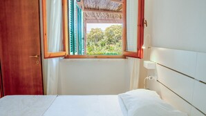Ein Schlafzimmer mit einem Bett, einem Fenster mit Vorhängen, einer Holztür und einer weißen Wand.