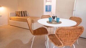 Ein stilvolles Wohnzimmer mit einem runden Esstisch, Korbstühlen, einer Couch und einer Kaffeestation.