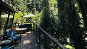 A wooden deck with outdoor seating and umbrellas, surrounded by tall trees. - Redwood Treehouse with Hot Tub (Guerneville)