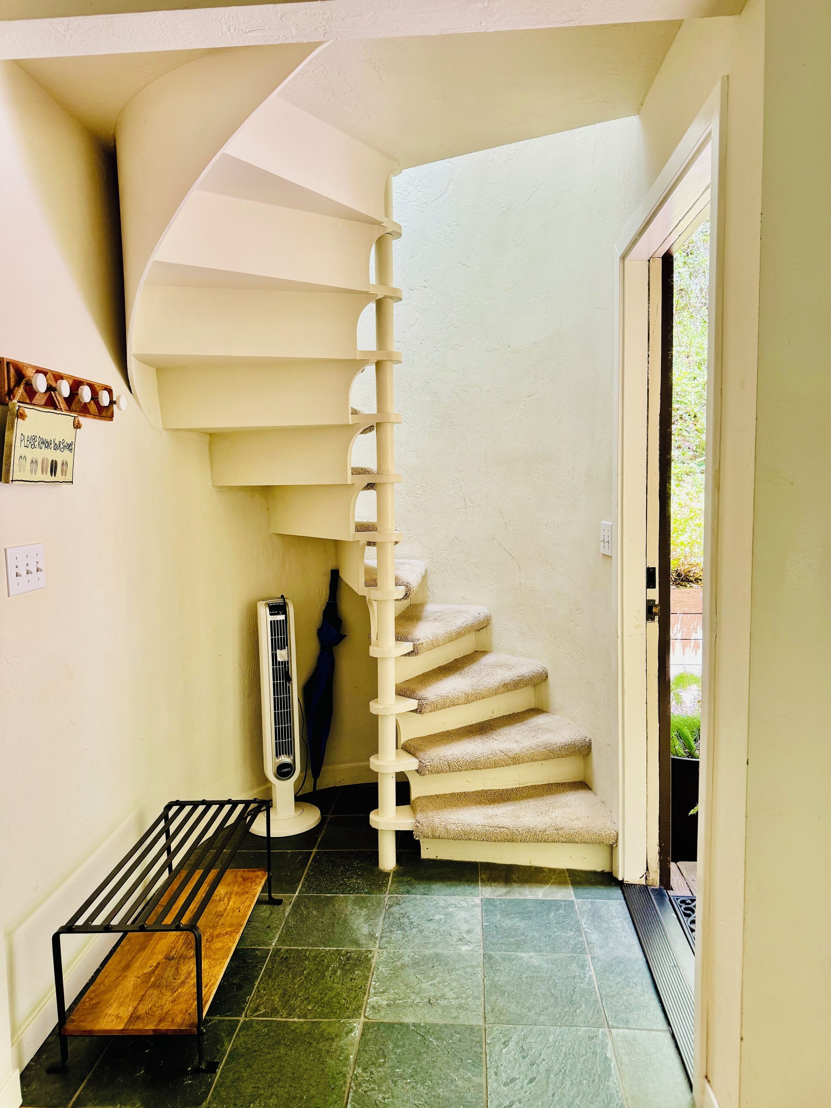 A spiral staircase with beige steps and a white handrail, leading to an upper floor.