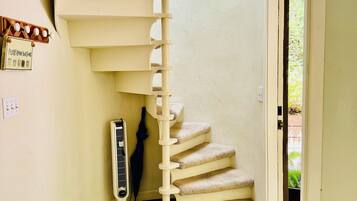 A spiral staircase with beige steps and a white handrail, leading to an upper floor.