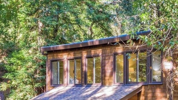 A two-story wooden cabin with large windows, a balcony, and a deck. - Redwood Treehouse with Hot Tub (Guerneville)