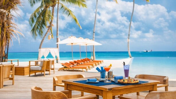 A beachside dining area with wooden tables and chairs, umbrellas, and a view of the ocean. - Penthouse at Hard Rock Hotel (Punta Cana)