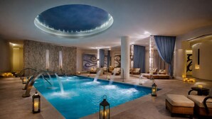 A spacious indoor pool area with a central pool, multiple lounge chairs, and ambient lighting. - Penthouse at Hard Rock Hotel (Punta Cana)