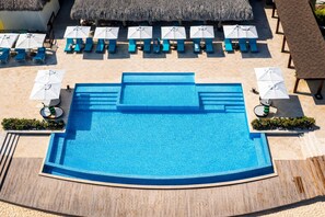 Een groot, helderblauw zwembad met een houten terras eromheen, voorzien van meerdere ligbedden en parasols.