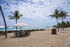 A beachside dining area with tables and chairs, white umbrellas, and palm trees. - Penthouse at the Hard Rock Hotel (Punta Cana)