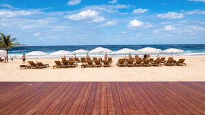A beach with wooden deck chairs and umbrellas, a palm tree, and the ocean. - Penthouse at Hard Rock Hotel (Punta Cana)