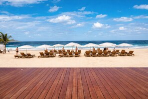 Ein Strand mit Holzliegen und Sonnenschirmen, eine Palme und das Meer.