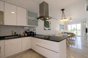 A modern kitchen with white cabinetry, a black countertop, and a central island. There is a large window providing natural light and a view of the outdoors. - Penthouse at the Hard Rock Hotel (Punta Cana)