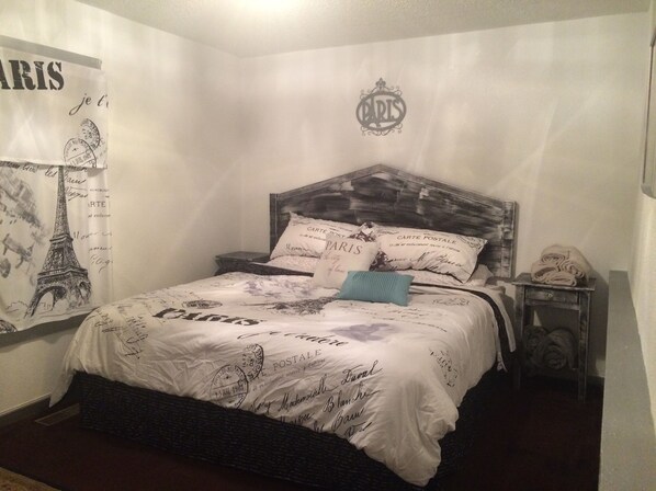 A bedroom with a bed featuring Paris-themed bedding, a headboard with a Paris logo, and a nightstand with a lamp. - Riverwalk Residences #2 (Lawrenceburg)