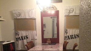 A dining area with a table covered by a Paris-themed tablecloth, flanked by chairs. A mirror hangs above the table, and the room has a vintage aesthetic with a clock on the wall. - Riverwalk Residences #2 (Lawrenceburg)