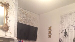Un salon avec un canapé gris, des coussins rouges, un téléviseur à écran plat fixé au mur, une petite table avec un vase et un tapis à motifs.