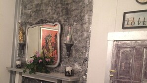 Une cheminée surmontée d’un miroir, une horloge au mur et un fauteuil moelleux placé en face.