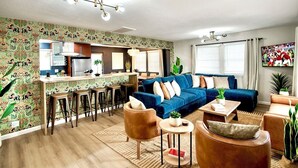 A modern living room with a blue sofa, a coffee table, and a kitchen area with bar stools. - Arcadia Retreat + Resort Yard + Hot Tub + Detached Casita (Phoenix)