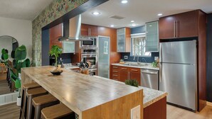 A modern kitchen with wooden cabinets, stainless steel appliances, and a central island with bar stools. - Arcadia Retreat + Resort Yard + Hot Tub + Detached Casita (Phoenix)