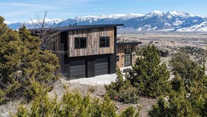 A modern two-story house with a garage, surrounded by trees and mountains in the background. - Moonrise Ridge, a Luxury Mountain Home set in Paradise Valley (Emigrant)