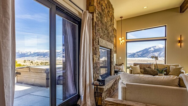 A spacious living room with a large window overlooking a mountainous landscape, a stone fireplace, and a cozy seating area. - Moonrise Ridge, a Luxury Mountain Home set in Paradise Valley (Emigrant)