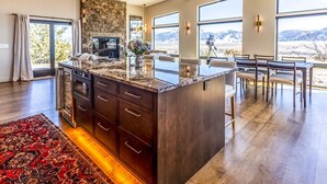 A spacious kitchen with a large island, wooden cabinets, and a stone backsplash. There are multiple windows offering views of the outdoors. - Moonrise Ridge, a Luxury Mountain Home set in Paradise Valley (Emigrant)