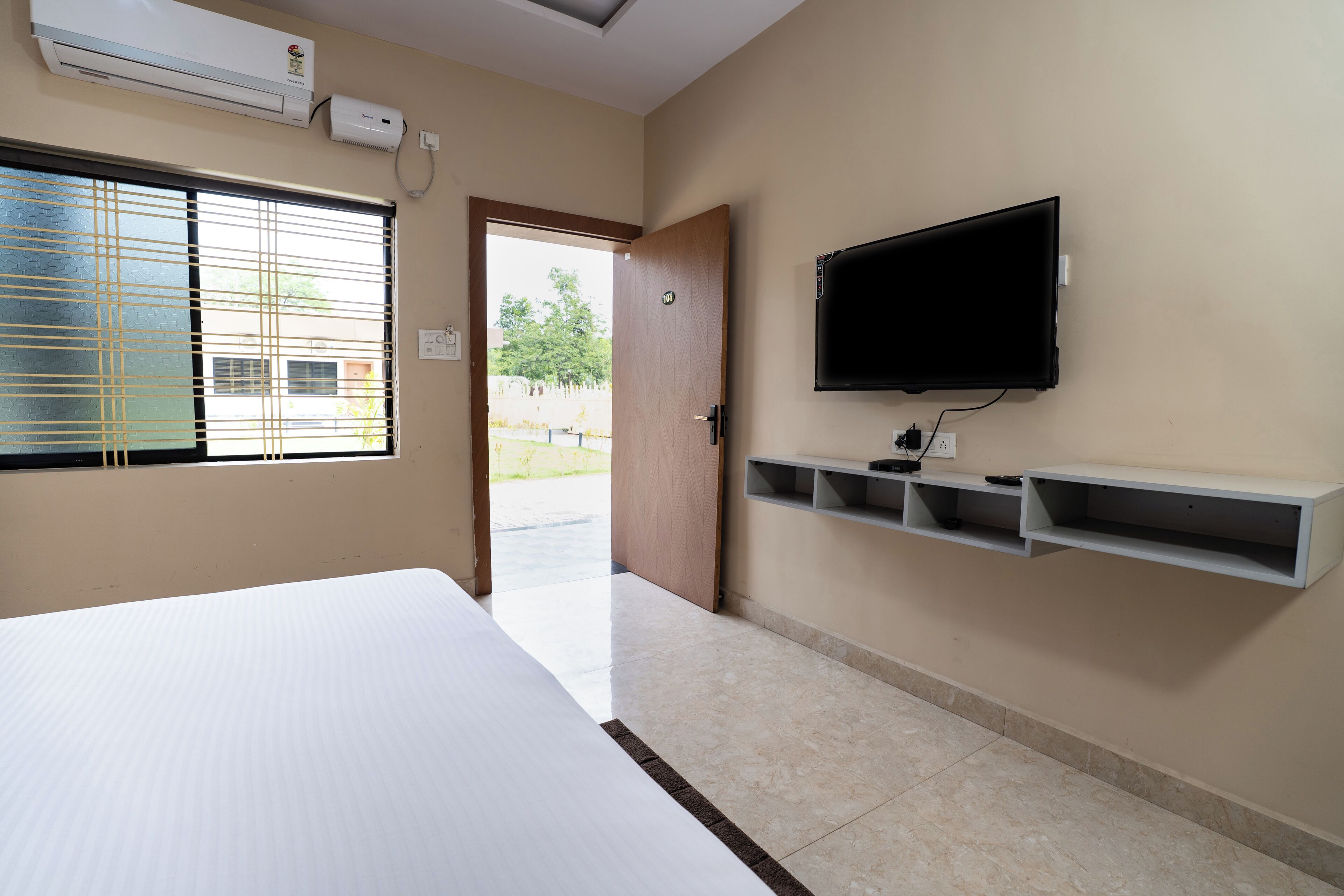 Une chambre d’hôtel équipée d’un lit, d’un téléviseur fixé au mur, d’une fenêtre avec des stores et d’un appareil de climatisation.