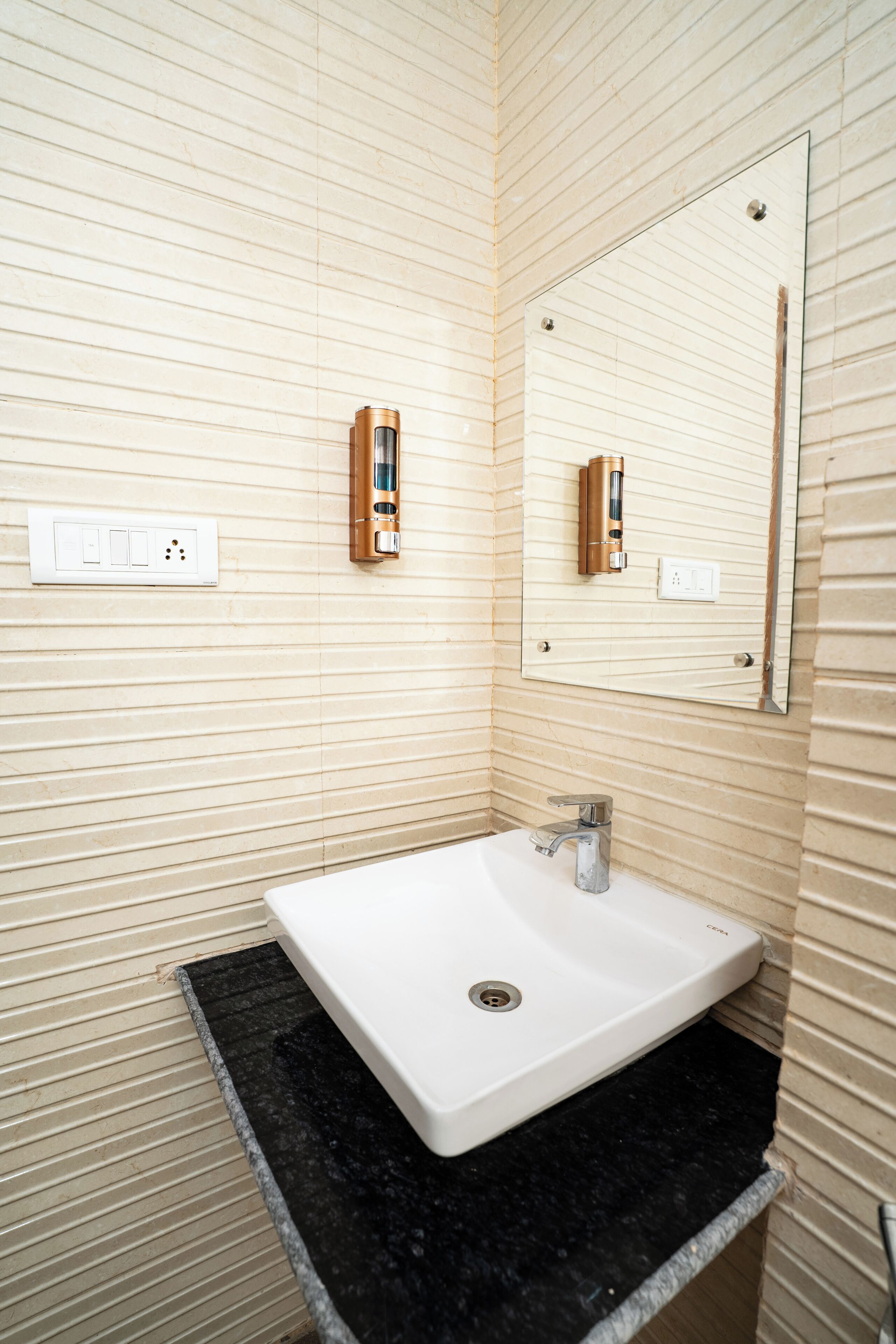 A bathroom with a white sink, a mirror, and a wall-mounted soap dispenser.