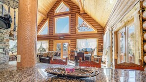 A log cabin interior with a stone wall, wooden ceiling, and a dining area with a table and chairs. - Custom high-end 3 bedroom log cabin sleeps 12. Located on the ski hill! (Angel Fire)