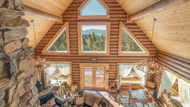 A log cabin interior with a stone wall, wooden ceiling, and a dining area with a table and chairs. - Custom high-end 3 bedroom log cabin sleeps 12. Located on the ski hill! (Angel Fire)