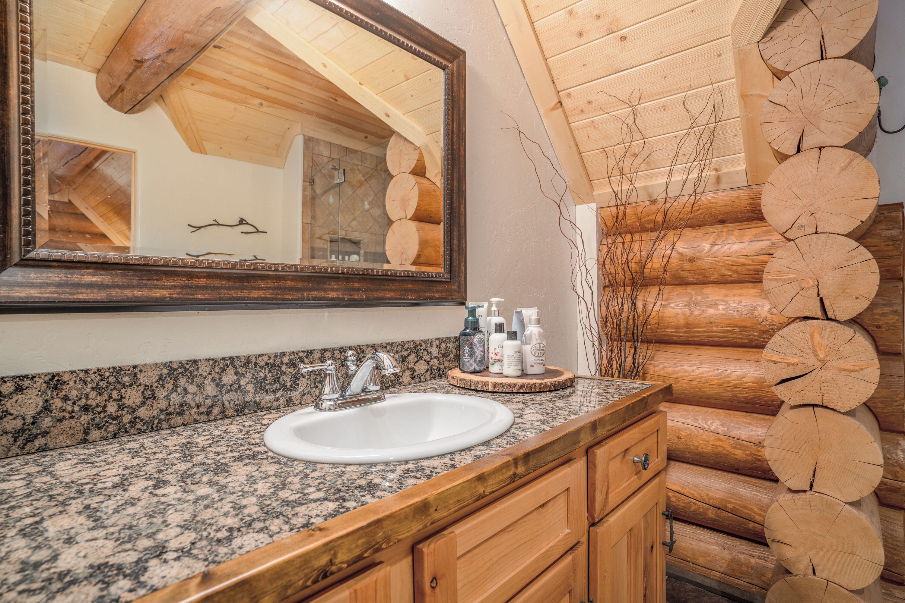 A bathroom with a granite countertop, a white sink, wooden cabinets, and a mirror with a wooden ceiling reflection.