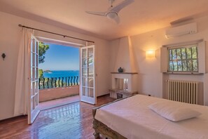 Een slaapkamer met een bed, een plafondventilator, een raam met uitzicht en een radiator.
