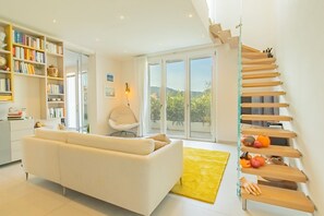 Una sala de estar moderna con un sofá blanco, una estantería, una silla y una escalera con cestas de fruta.