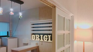 A modern kitchen with a white countertop, two stools, and a wall-mounted light sign that reads "ORIGI".