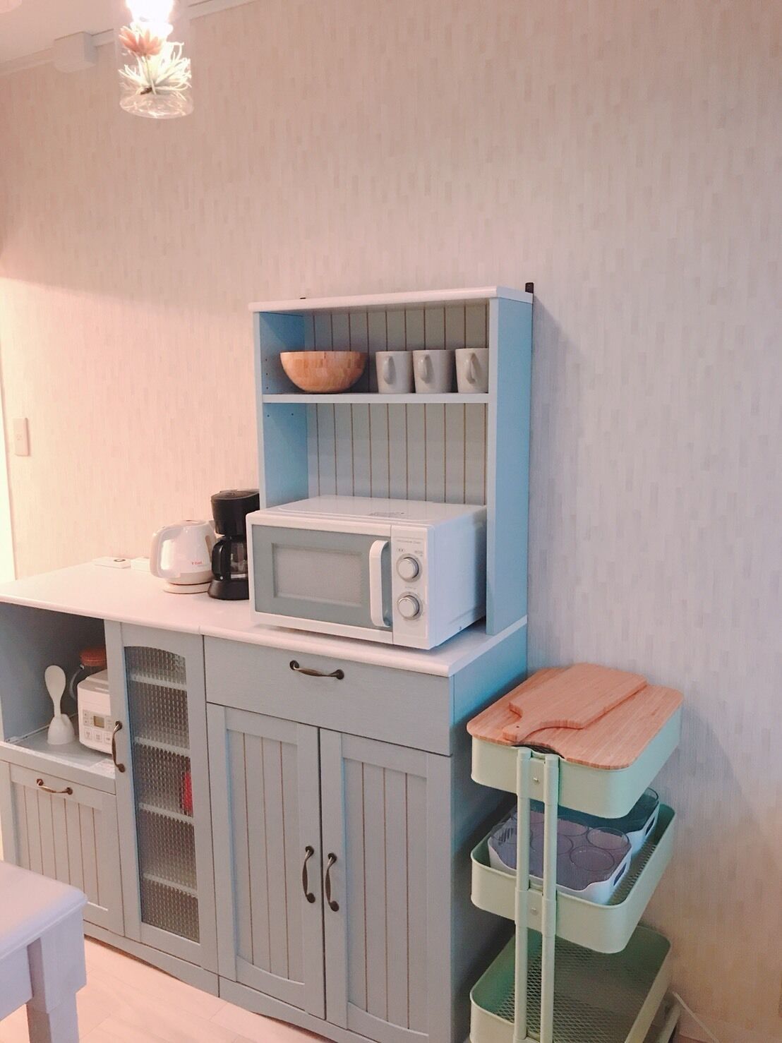 A kitchen with a microwave, kettle, and storage shelves.