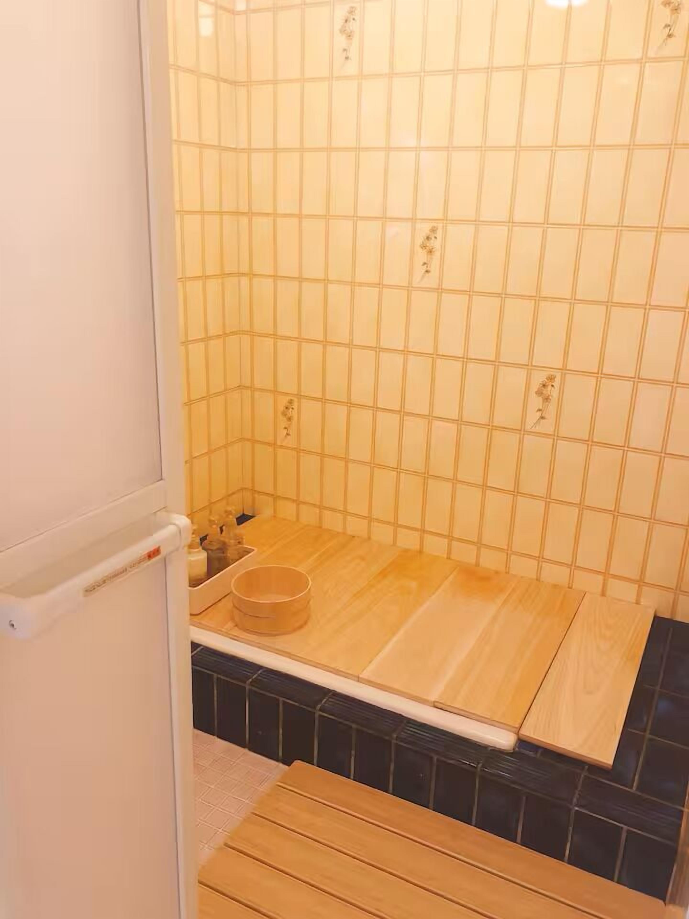 Un área de ducha pequeña con azulejos, un banco de madera y una sola botella de champú.