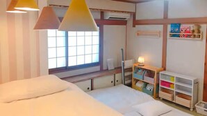 A bedroom with a bed, two pendant lights, a window, a radiator, and storage shelves.