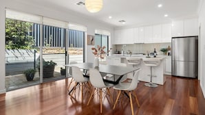 A modern kitchen with white cabinets, a stainless steel refrigerator, and a dining area with a table and chairs. - St Georges Gem—Spacious & Well-located Family Stay (Saint Georges)