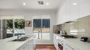 A modern kitchen with white cabinets, a stainless steel sink, and a gas stove. - St Georges Gem—Spacious & Well-located Family Stay (Saint Georges)