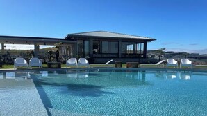 Une piscine aux eaux cristallines, avec des chaises longues, et un bâtiment moderne en arrière-plan.