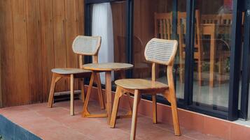 Two wooden chairs with woven seats and legs, placed on a tiled patio outside a building with large windows.
