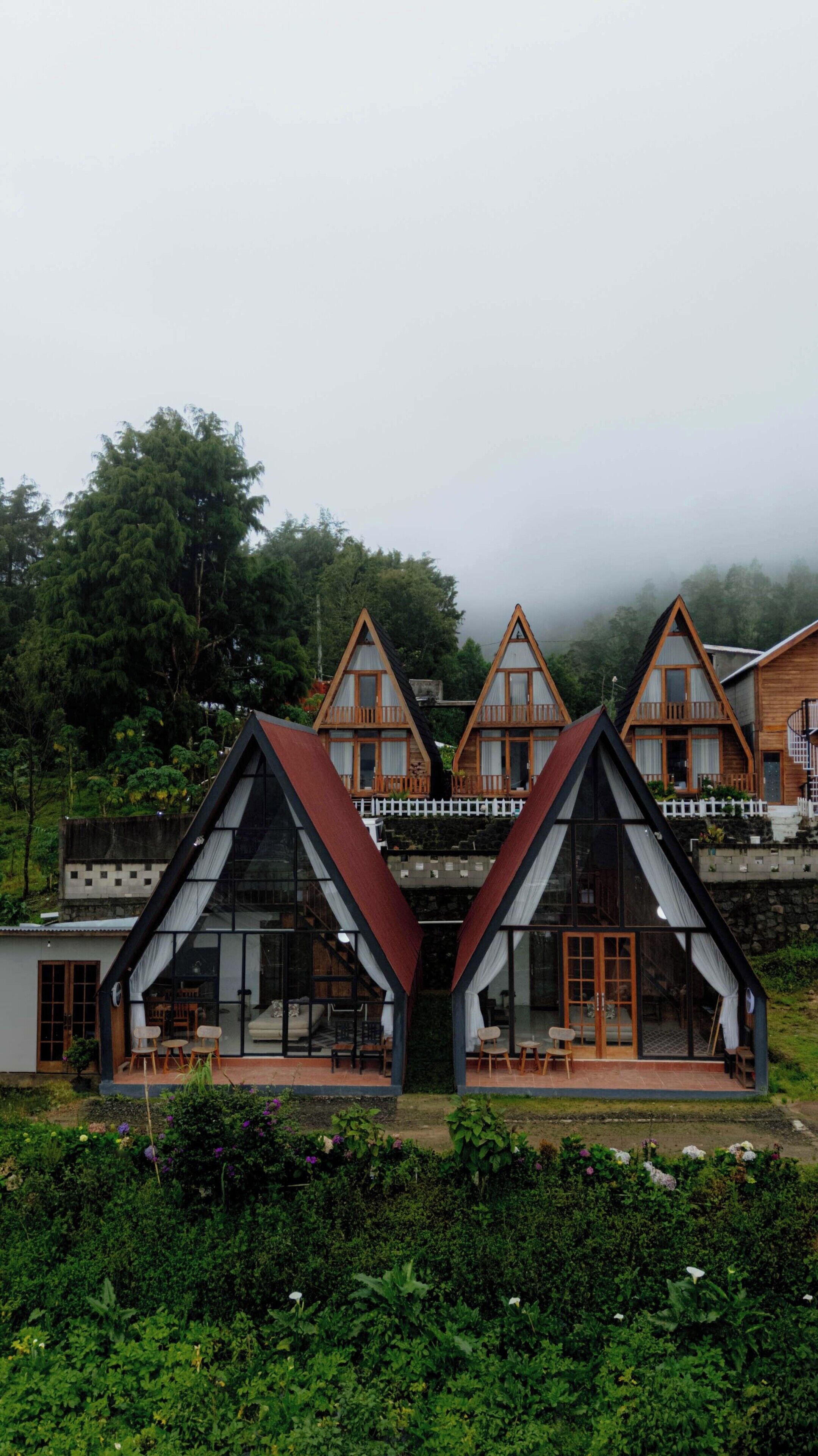 A row of A-frame cabins with glass doors and windows, surrounded by lush greenery.
