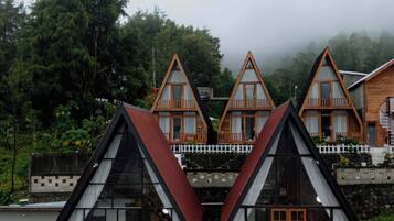 A row of A-frame cabins with glass doors and windows, surrounded by lush greenery.