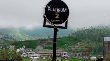 Schild für Villa Platinum DIENG 2 mit Blick auf gestufte Felder und Häuser im Hintergrund.