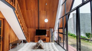 A modern interior with a wooden ceiling, a sofa, a television, and large windows. - Villa Platinum 2 (Dieng Kulon)