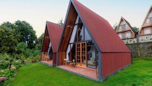 A modern, triangular-shaped building with large windows and a red roof, surrounded by a well-maintained garden. - Villa Platinum 2 (Dieng Kulon)