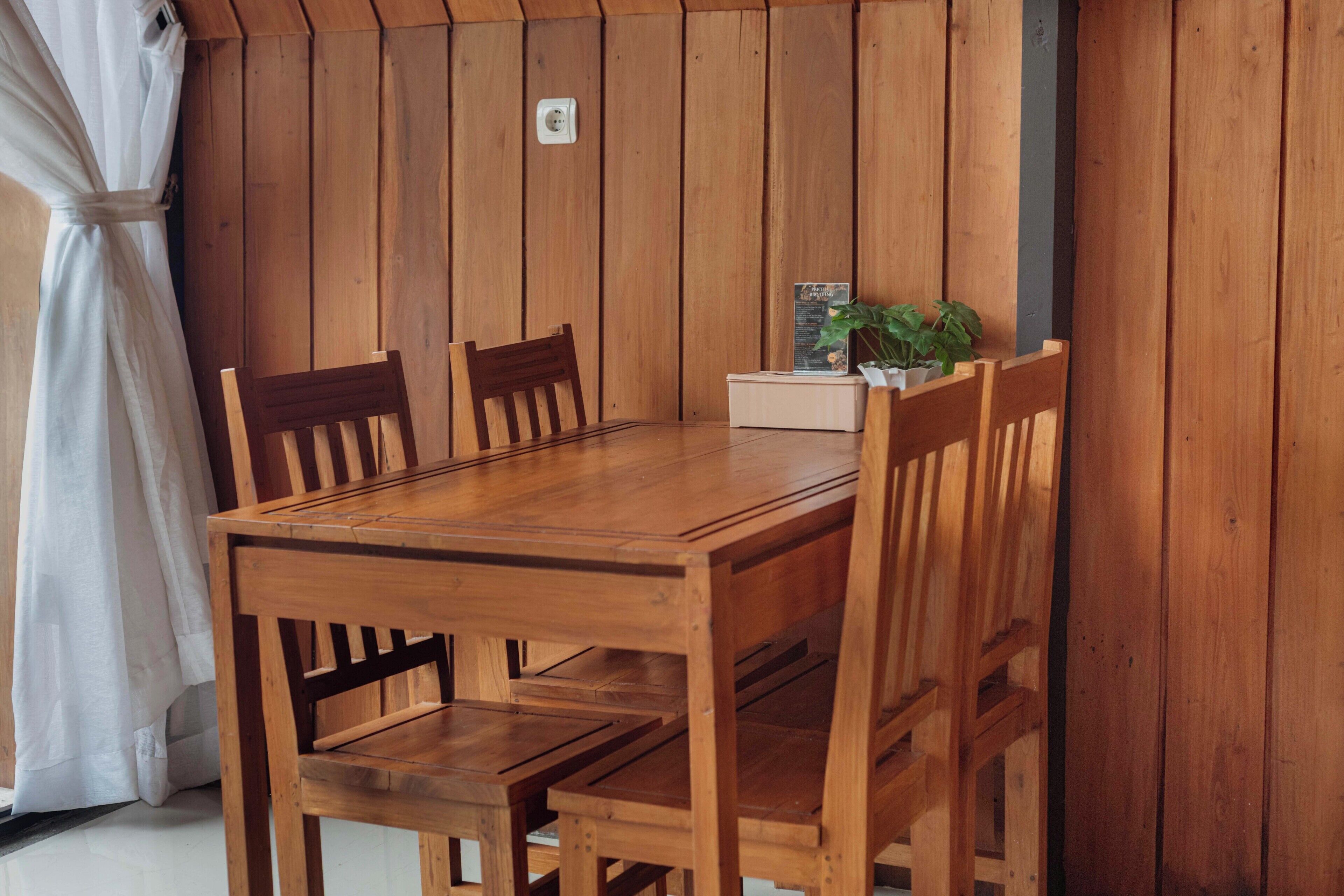 Une table à manger en bois, accompagnée de quatre chaises, d’une petite plante et d’un présentoir à menus.