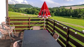A wooden deck with wicker chairs and a table, overlooking a green landscape with a red umbrella. - Green Valley Park Stárkov 9 by Interhome (Stárkov)