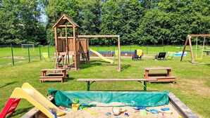 A playground with a wooden play structure, picnic tables, and a sandpit. - Green Valley Park Stárkov 9 by Interhome (Stárkov)