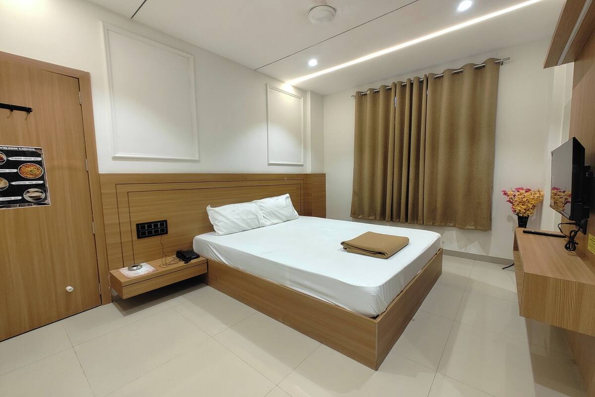 A hotel room with a wooden bed, a bedside table, a TV, and a curtain.